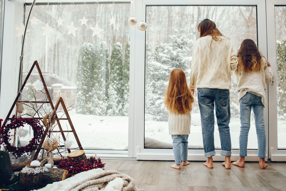 Familie schaut vom Fenster in den winterlichen Garten